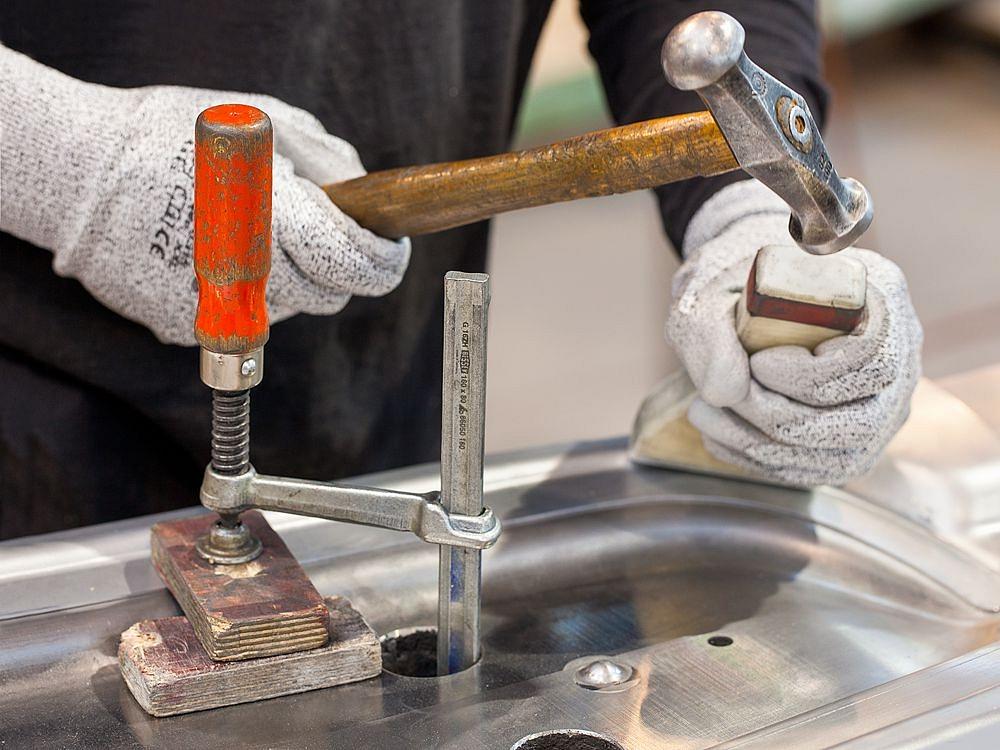 Close-up of manual processing of a metal prototype using a hammer and clamping tool